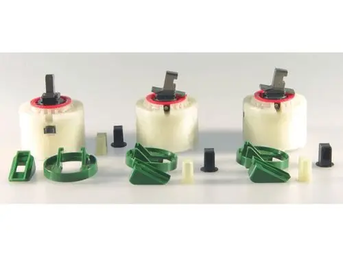 Drei Click-Kartuschen von Ideal Standard, jeweils mit einem schwarzen Griff und verschiedenen Halterungen. Umgeben von mehreren kleinen Kunststoffteilen in unterschiedlichen Formen.